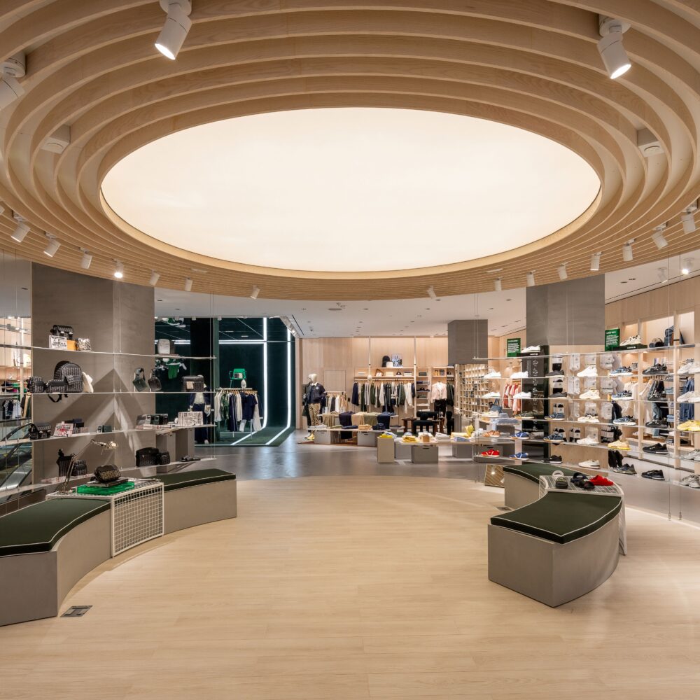 Second-floor interior of Lacoste Flagship Store, Fifth Avenue, New York, featuring circular ceiling lighting by Zeplinn highlighting products displayed around the space.